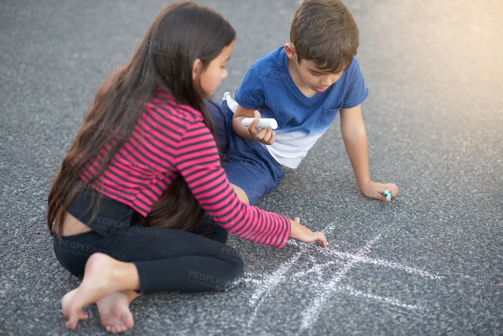 Buy stock photo Shot of a cute little boy playing tic tac toe with his sister on the pavement outside their house