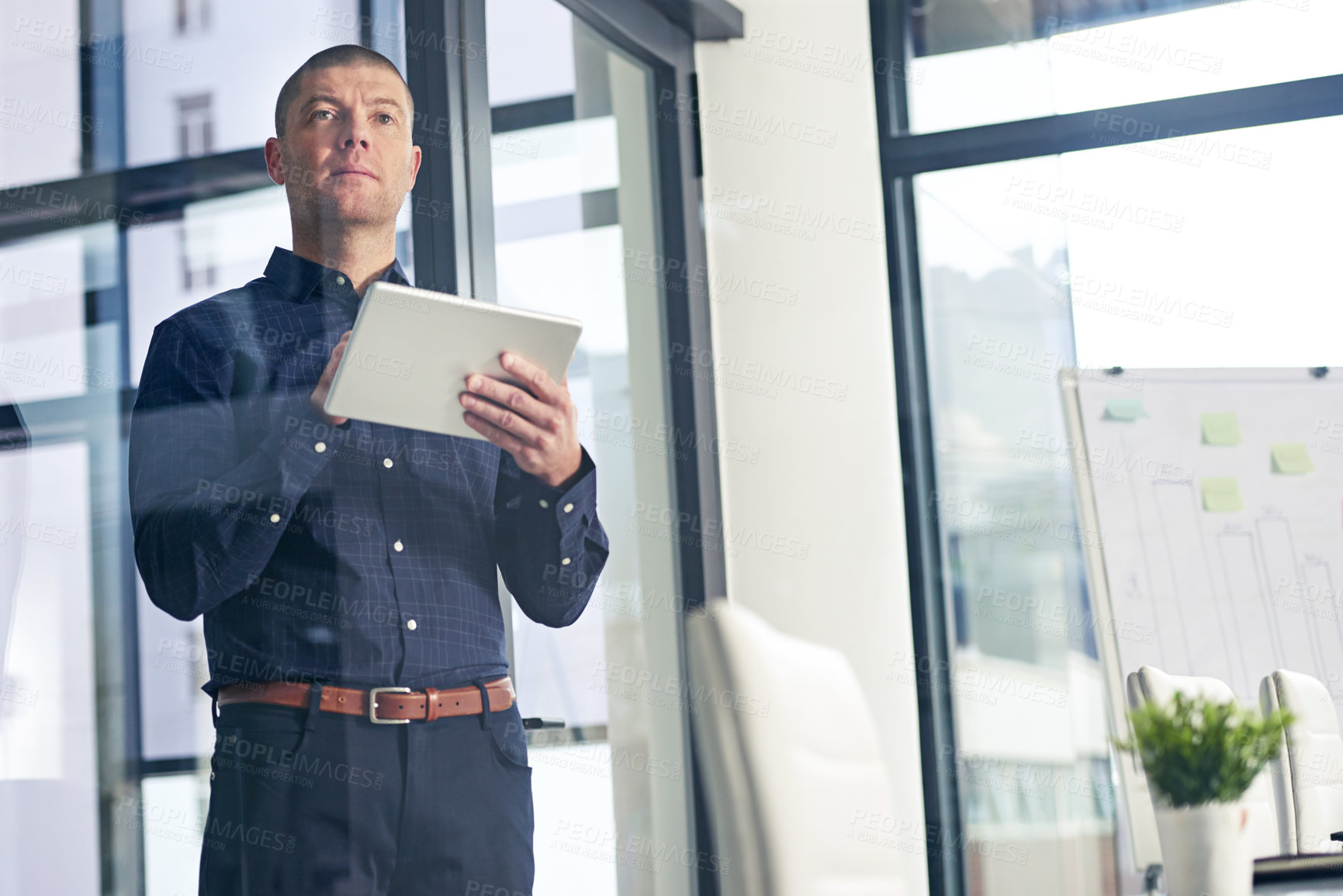 Buy stock photo Shot of a thoughtful businessman using a digital tablet in a modern office
