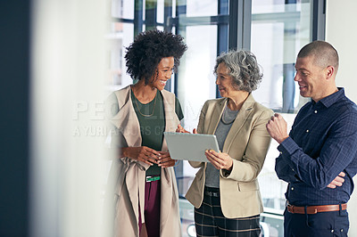 Buy stock photo Shot of a team of colleagues using a digital tablet during an informal meeting