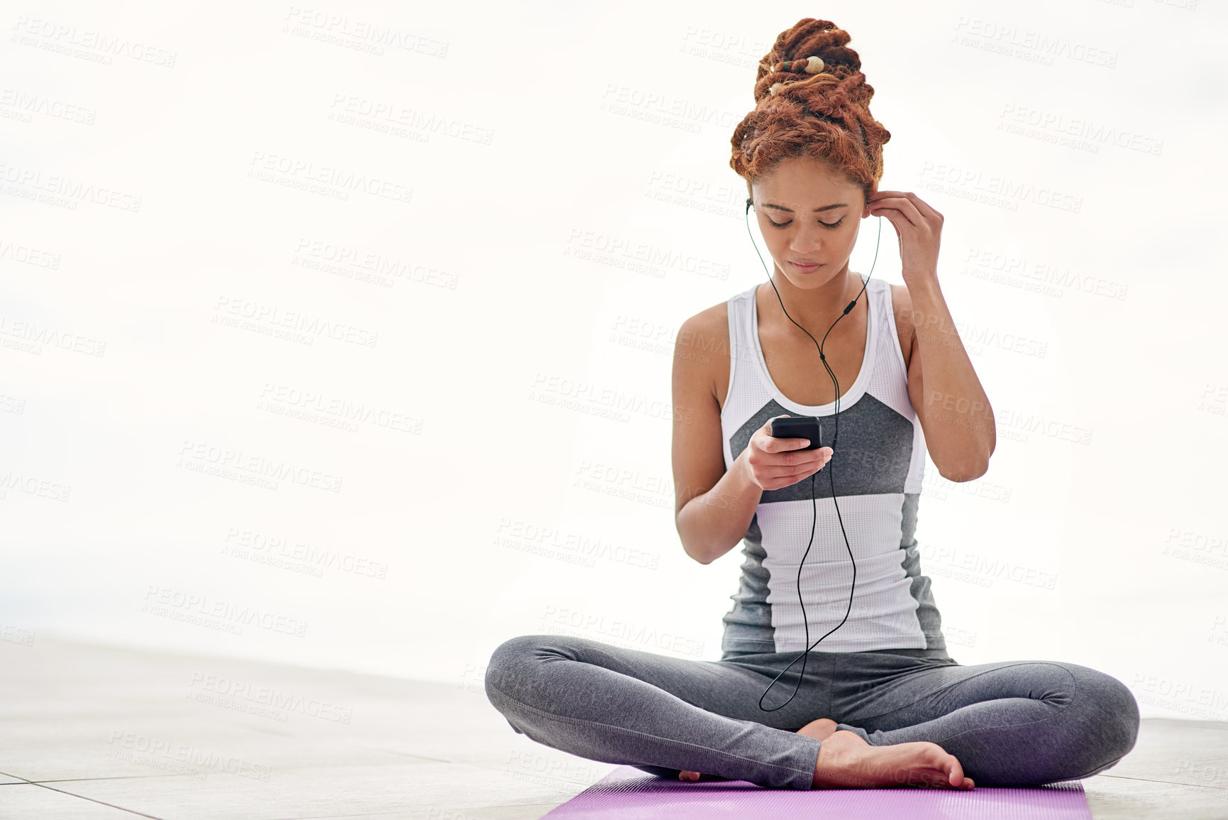 Buy stock photo Shot of a young woman listening to music while practicing yoga outside