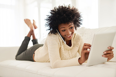 Buy stock photo Shot of an attractive young using her cellphone and tablet while lying on the sofa at home