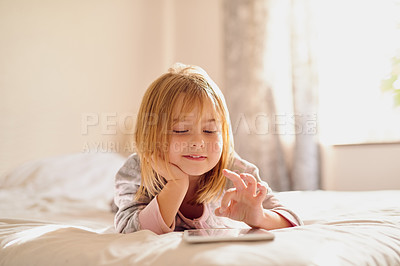 Buy stock photo Shot of a little girl playing with her tablet while lying on her bed at home