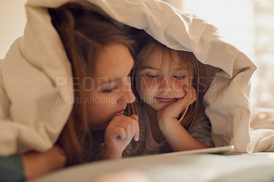 Buy stock photo Shot of a mother and her little girl looking at a tablet together while lying under a blanket