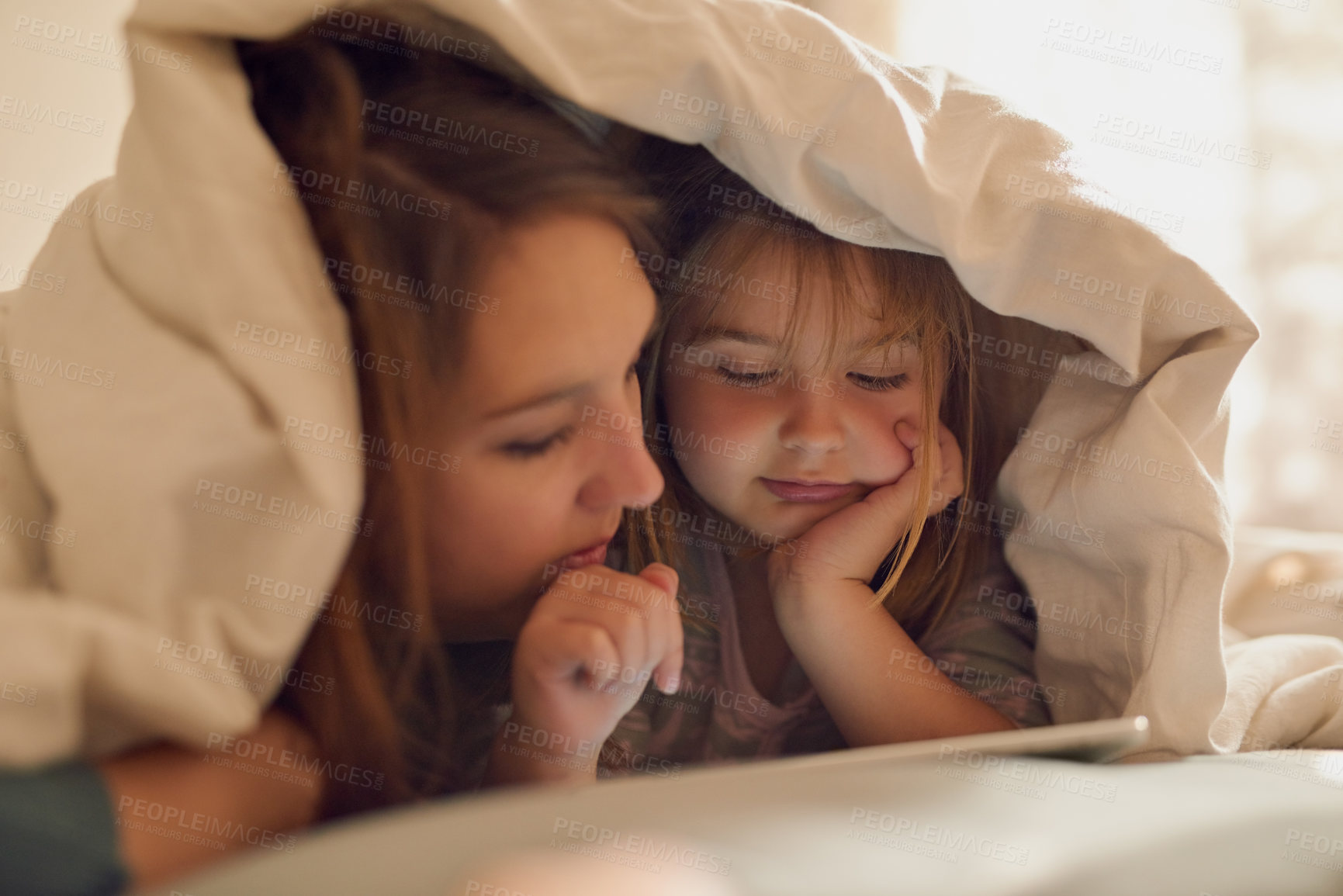 Buy stock photo Shot of a mother and her little girl looking at a tablet together while lying under a blanket