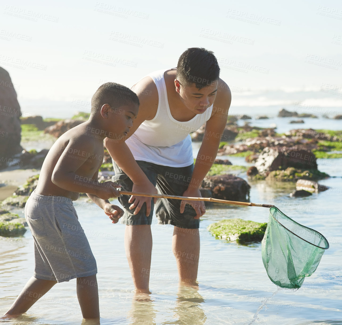 Buy stock photo Shot of a father and his young son fishing with a net at the beach