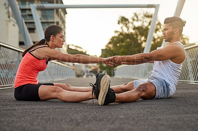 Buy stock photo Shot of a young couple warming up on a bridge before their workout