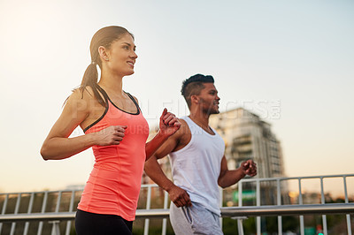 Buy stock photo Shot of a young couple crossing a bridge during their run