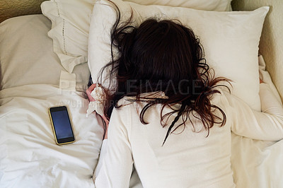 Buy stock photo High angle shot of a young woman lying in bed with tissues and her cellphone next to her