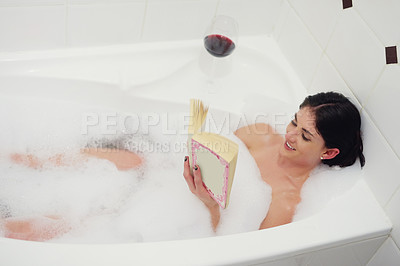 Buy stock photo Cropped shot of a young woman relaxing in the bathtub with a book and glass of wine