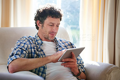Buy stock photo Shot of a mature man using his tablet while sitting on the sofa at home