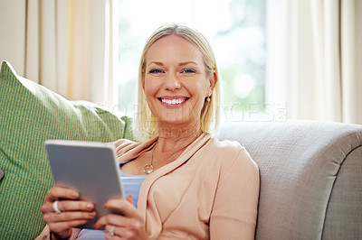 Buy stock photo Portrait of a mature woman using her tablet while sitting on the sofa at home
