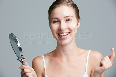 Buy stock photo Studio portrait of an attractive young woman holding a hand mirror and applying cosmetics against a gray background