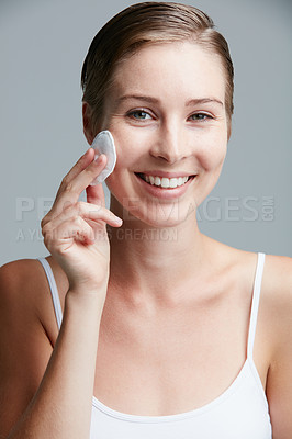 Buy stock photo Studio portrait of an attractive young woman using a cotton pad on her face against a gray background