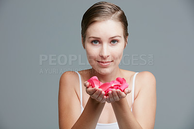 Buy stock photo Studio portrait of an attractive young woman holding a handful of pink petals against a gray background