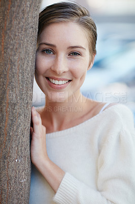Buy stock photo Portrait of a smiling young woman leaning against a tree outside
