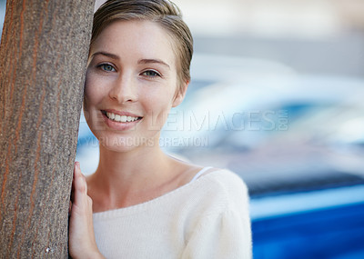Buy stock photo Portrait of a smiling young woman leaning against a tree outside