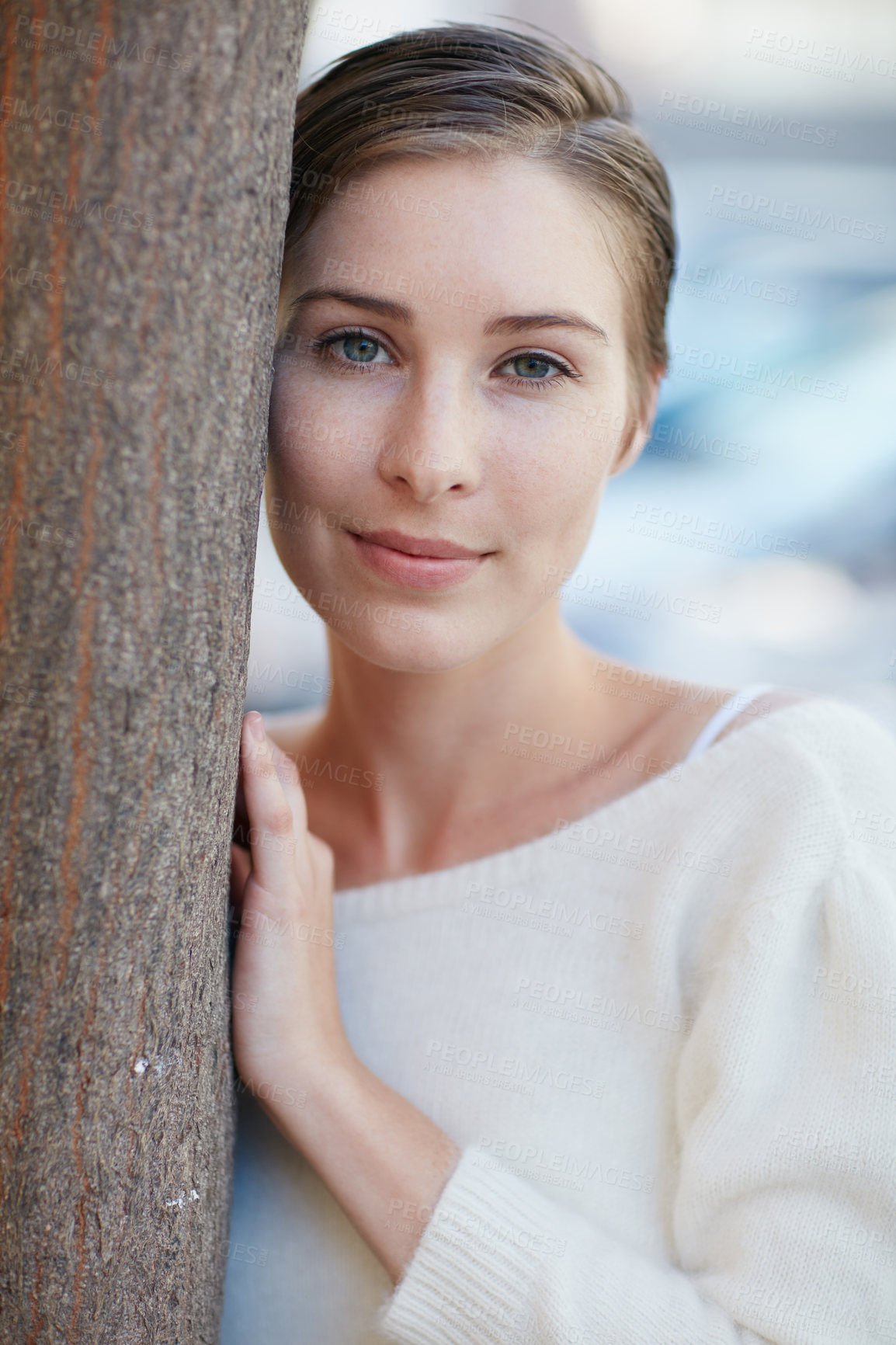 Buy stock photo Portrait of a smiling young woman leaning against a tree outside