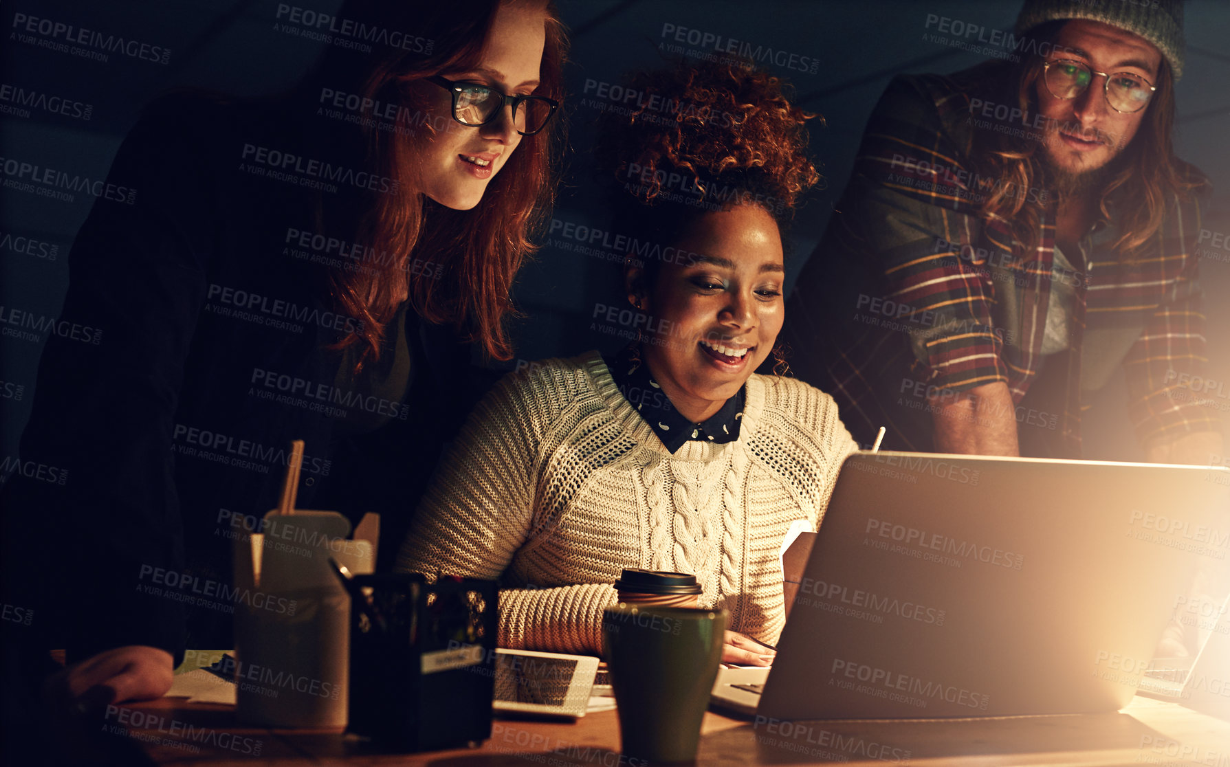 Buy stock photo Shot of a business team using a laptop together on a night shift at work