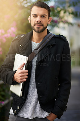 Buy stock photo Shot of a handsome young man standing outdoors and holding a laptop