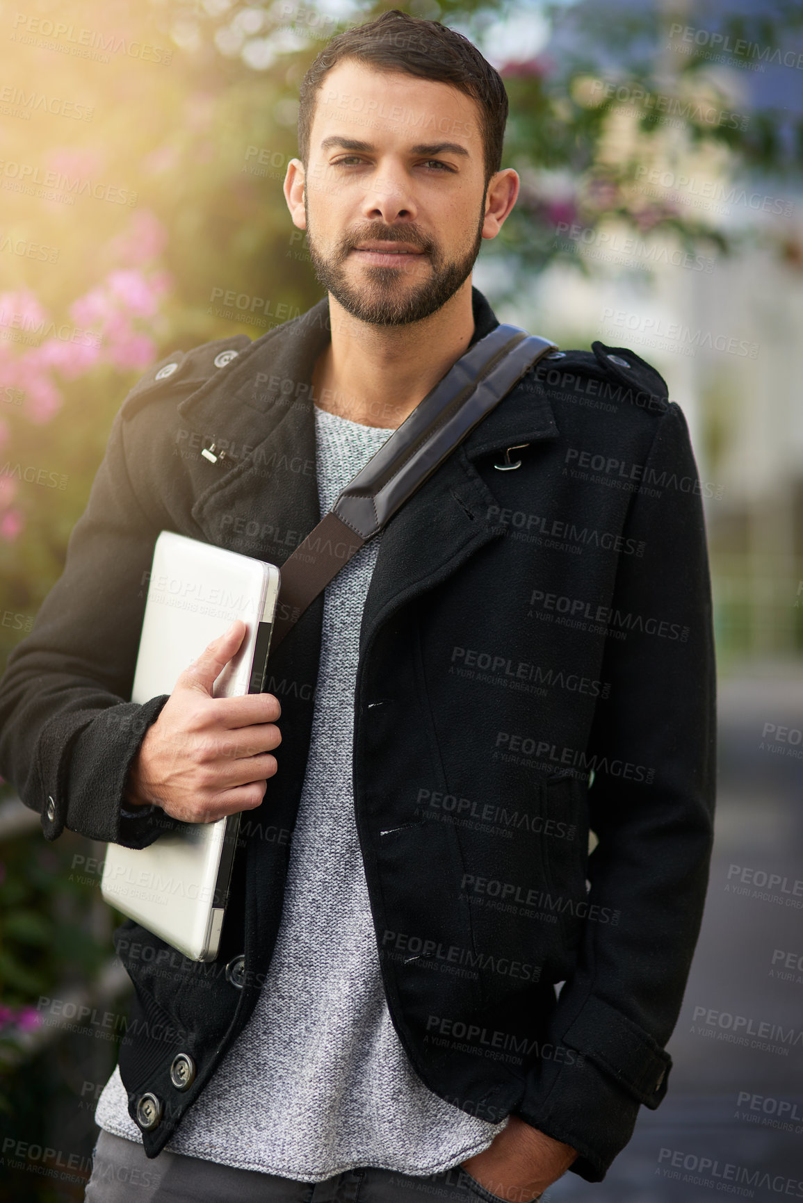 Buy stock photo Shot of a handsome young man standing outdoors and holding a laptop