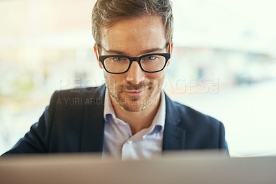 Buy stock photo Shot of a young businessman using his laptop while sitting in a coffee shop