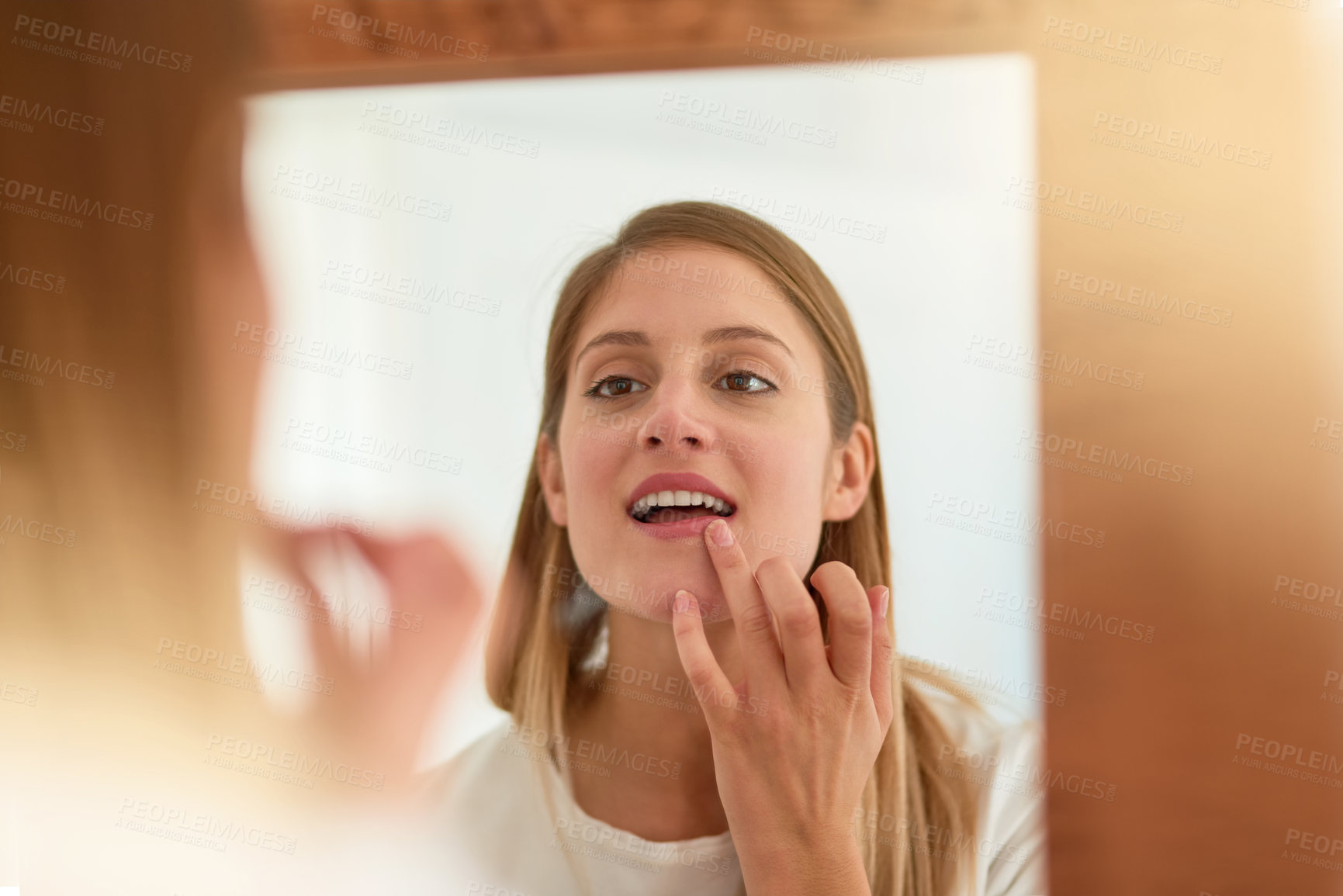 Buy stock photo Shot of a young woman touching up her lipstick in front of a mirror at home