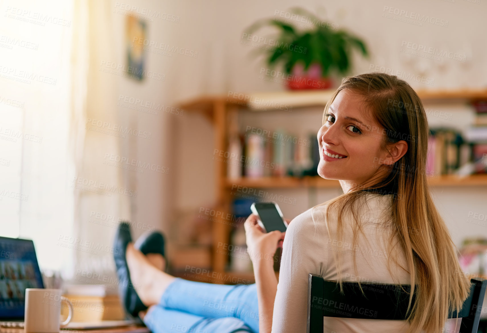 Buy stock photo Portrait of a young woman using her smartphone while sitting at her desk at home