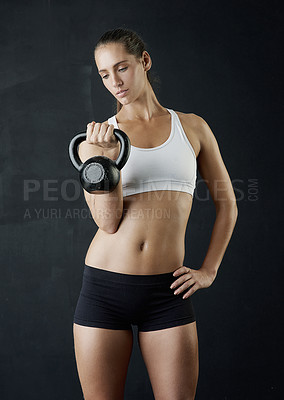 Buy stock photo Studio shot of an attractive young woman working out with a kettle bell against a dark background