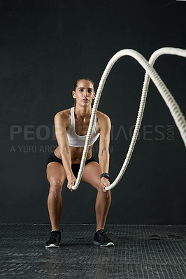 Buy stock photo Studio shot of an attractive young woman working out with heavy ropes against a dark background