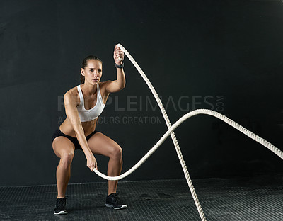 Buy stock photo Studio shot of an attractive young woman working out with heavy ropes against a dark background