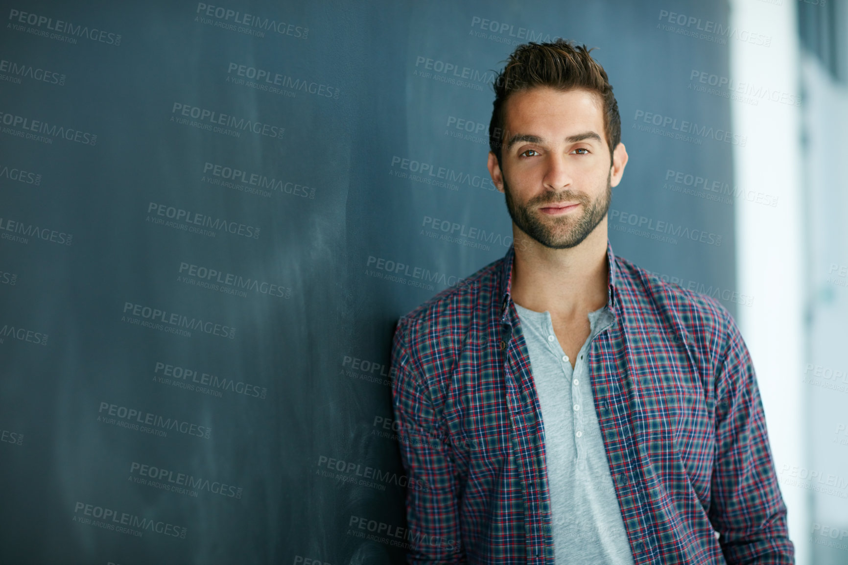 Buy stock photo Portrait of a confident young man leaning against a blackboard