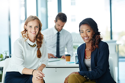 Buy stock photo Portrait of two businesswomen sitting in an office with a colleague in the background