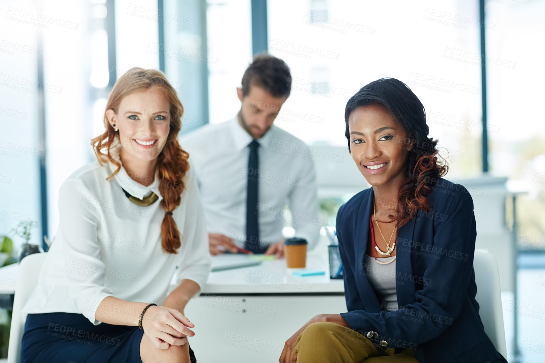 Buy stock photo Portrait of two businesswomen sitting in an office with a colleague in the background