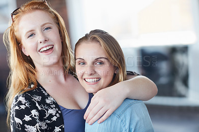 Buy stock photo Portrait of two university students embracing while standing in their classroom