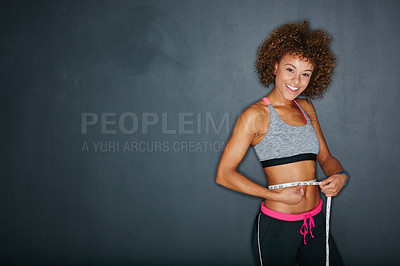 Buy stock photo Portrait of a sporty young woman measuring her waist against a grey background