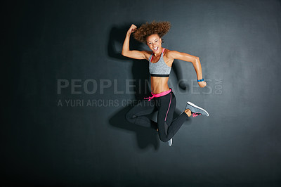 Buy stock photo Shot of a young woman flexing her muscles while jumping against a grey background