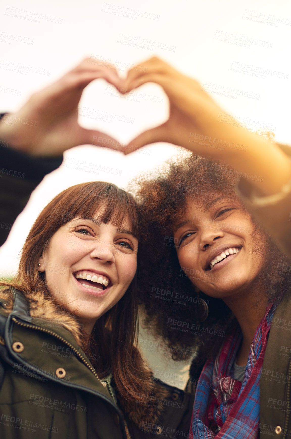 Buy stock photo Shot of two friends making a heart shape with their hands while standing outside