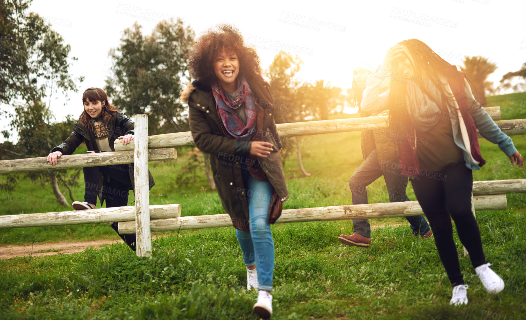 Buy stock photo Shot of a group of friends jumping over a fence in a field for fun