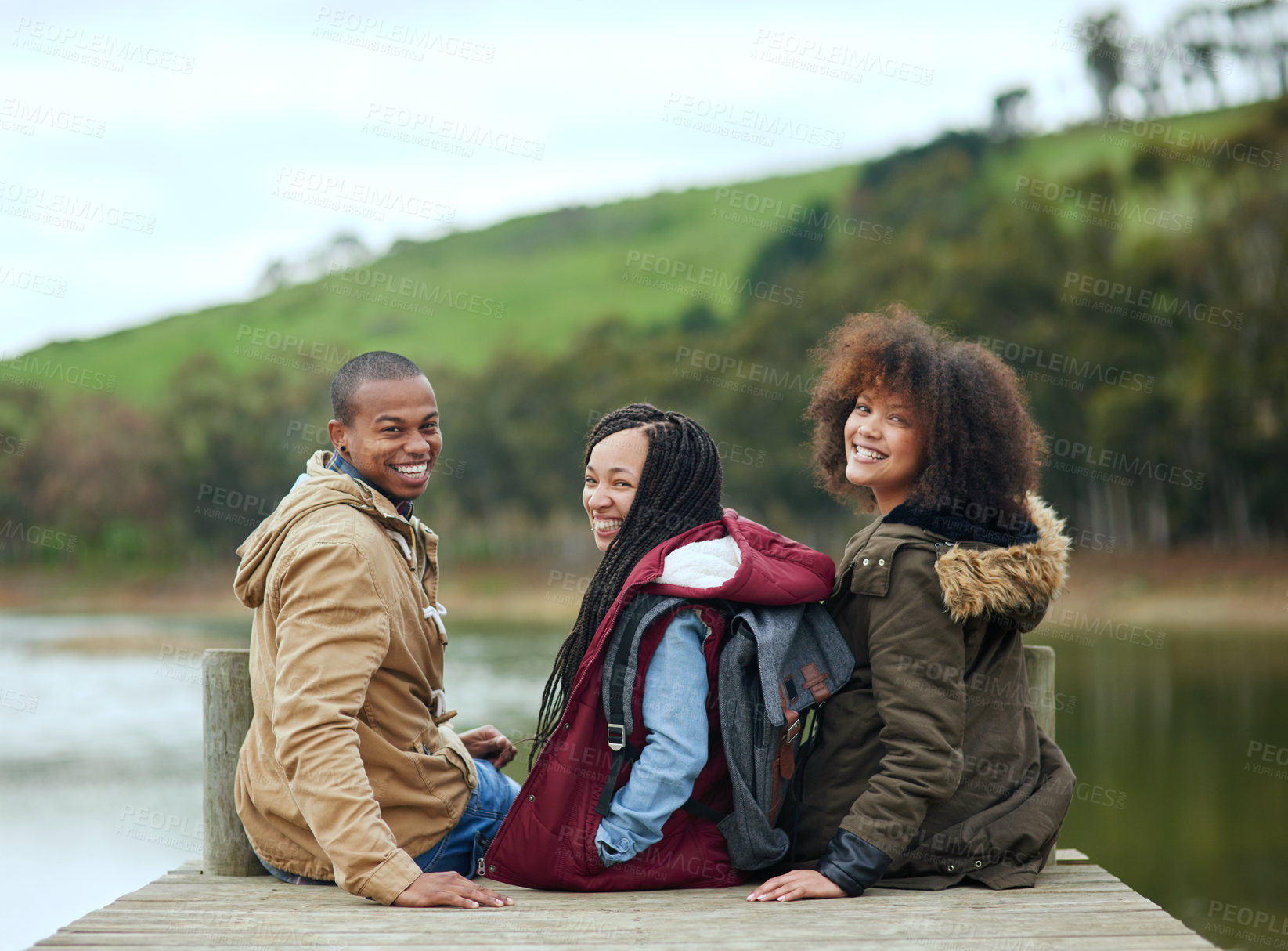 Buy stock photo Portrait of a group of friends looking over their shoulders while sitting on a pier together