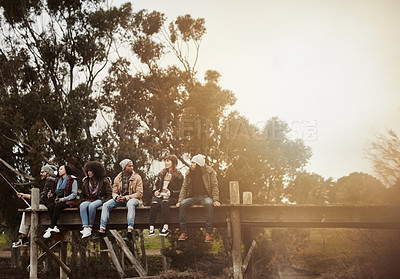 Buy stock photo Shot of a group of friends sitting on a pier together on a weekend breakaway