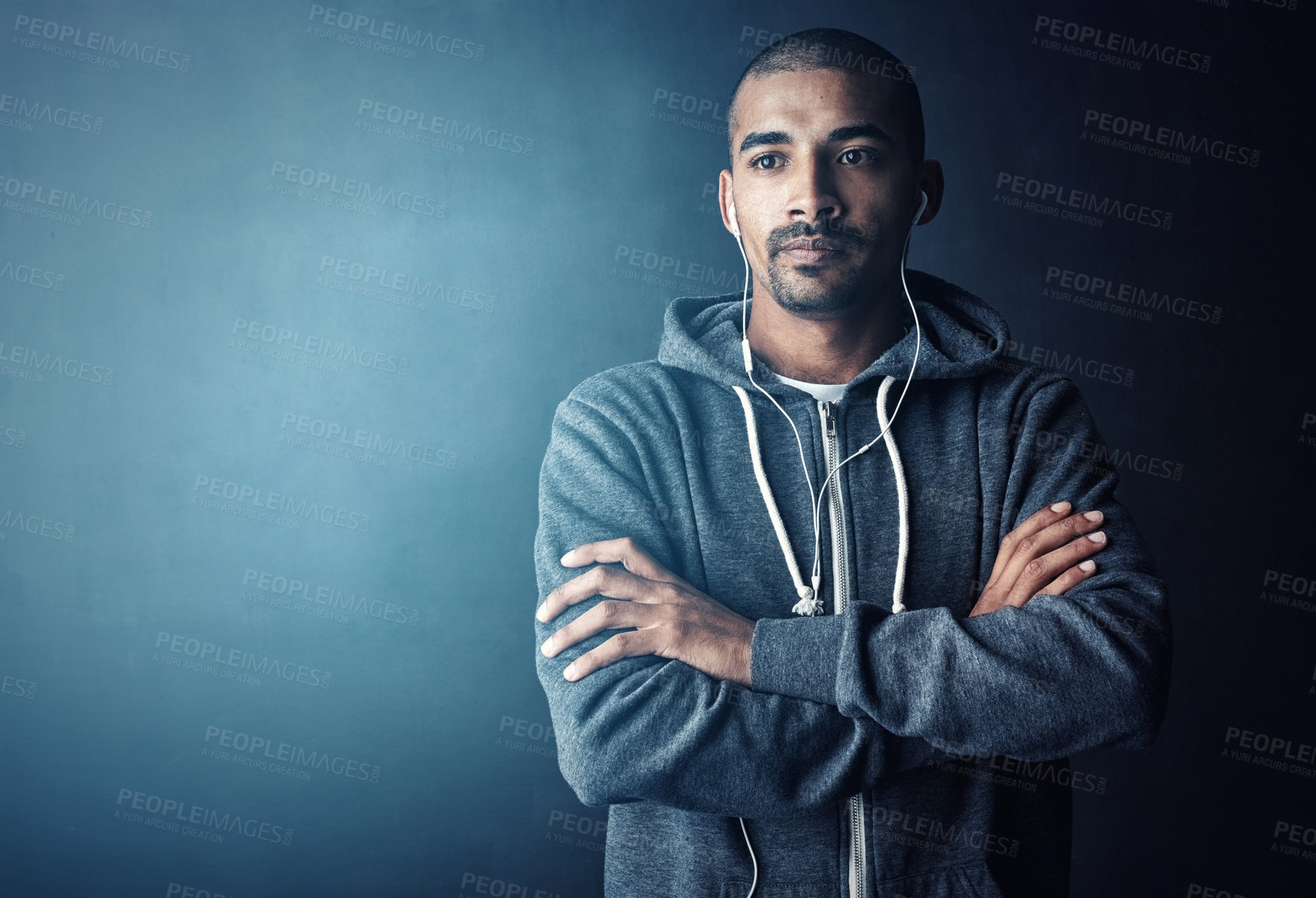 Buy stock photo Studio shot of a young man standing with his arms folded against a dark background
