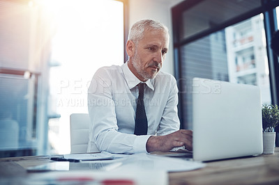 Buy stock photo Shot of a businessman sitting at his office desk working on a laptop