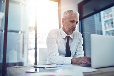 Buy stock photo Shot of a businessman sitting at his office desk working on a laptop