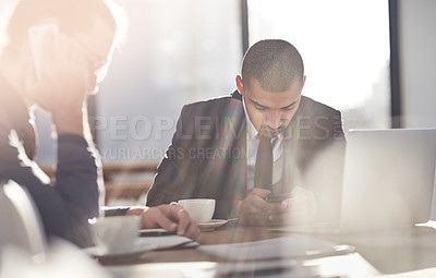 Buy stock photo Shot of two young businessmen using their smartphones at work