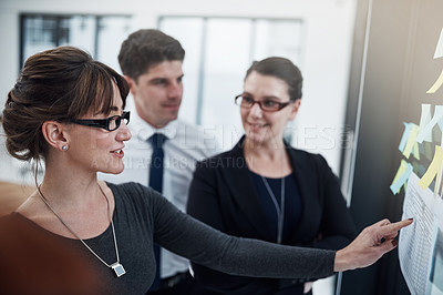 Buy stock photo Cropped shot of a group of businesspeople brainstorming with notes on a glass wall in an office