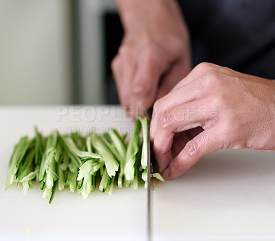 Buy stock photo Shot of an unidentifiable young man slicing vegetables in his kitchen
