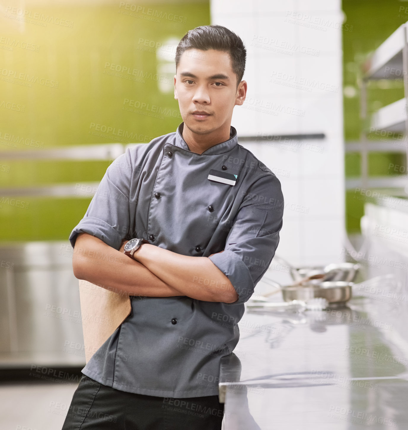 Buy stock photo Cropped portrait of a young male chef standing with his arms folded in the kitchen