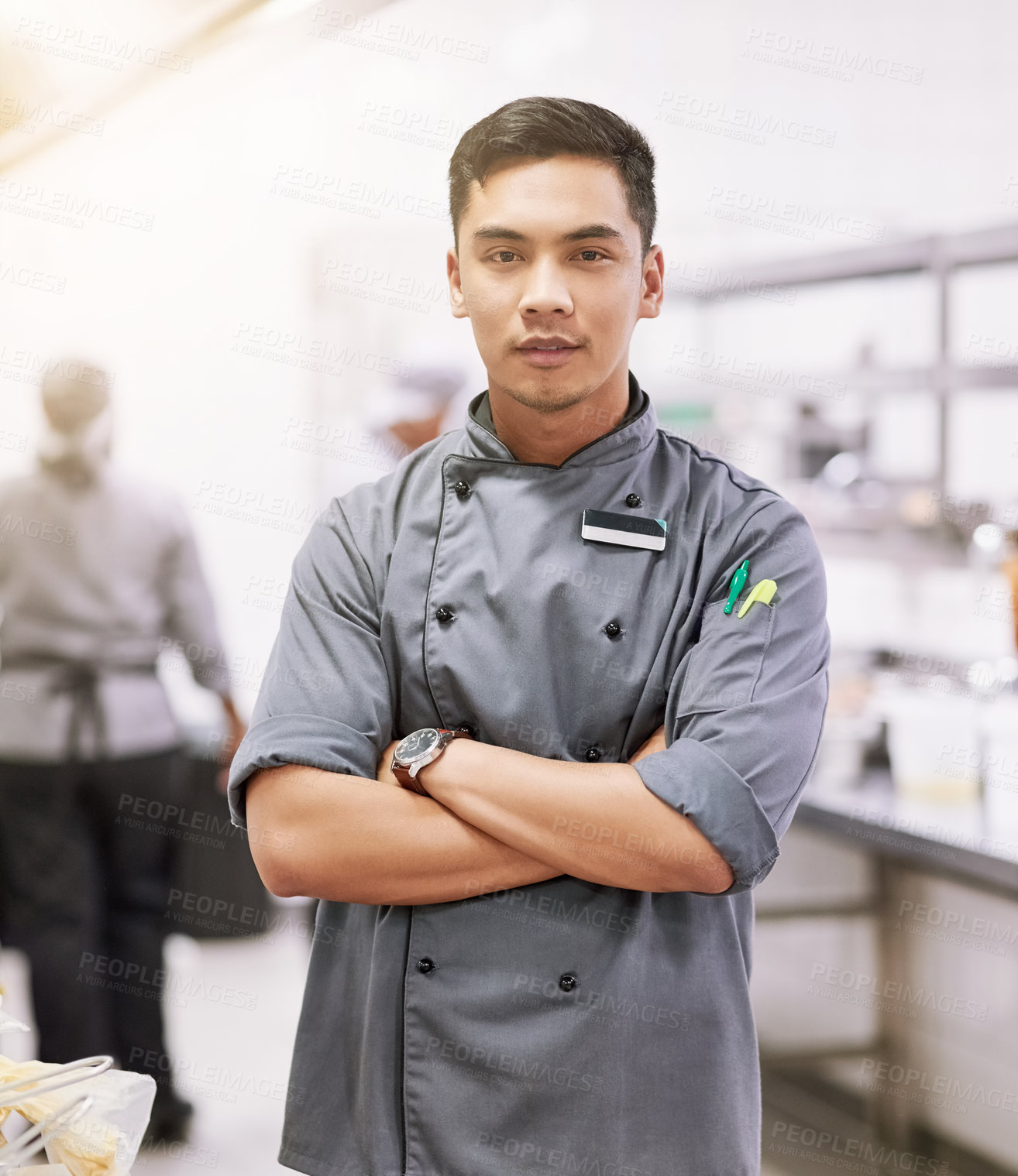 Buy stock photo Cropped portrait of a young male chef standing with his arms folded in the kitchen