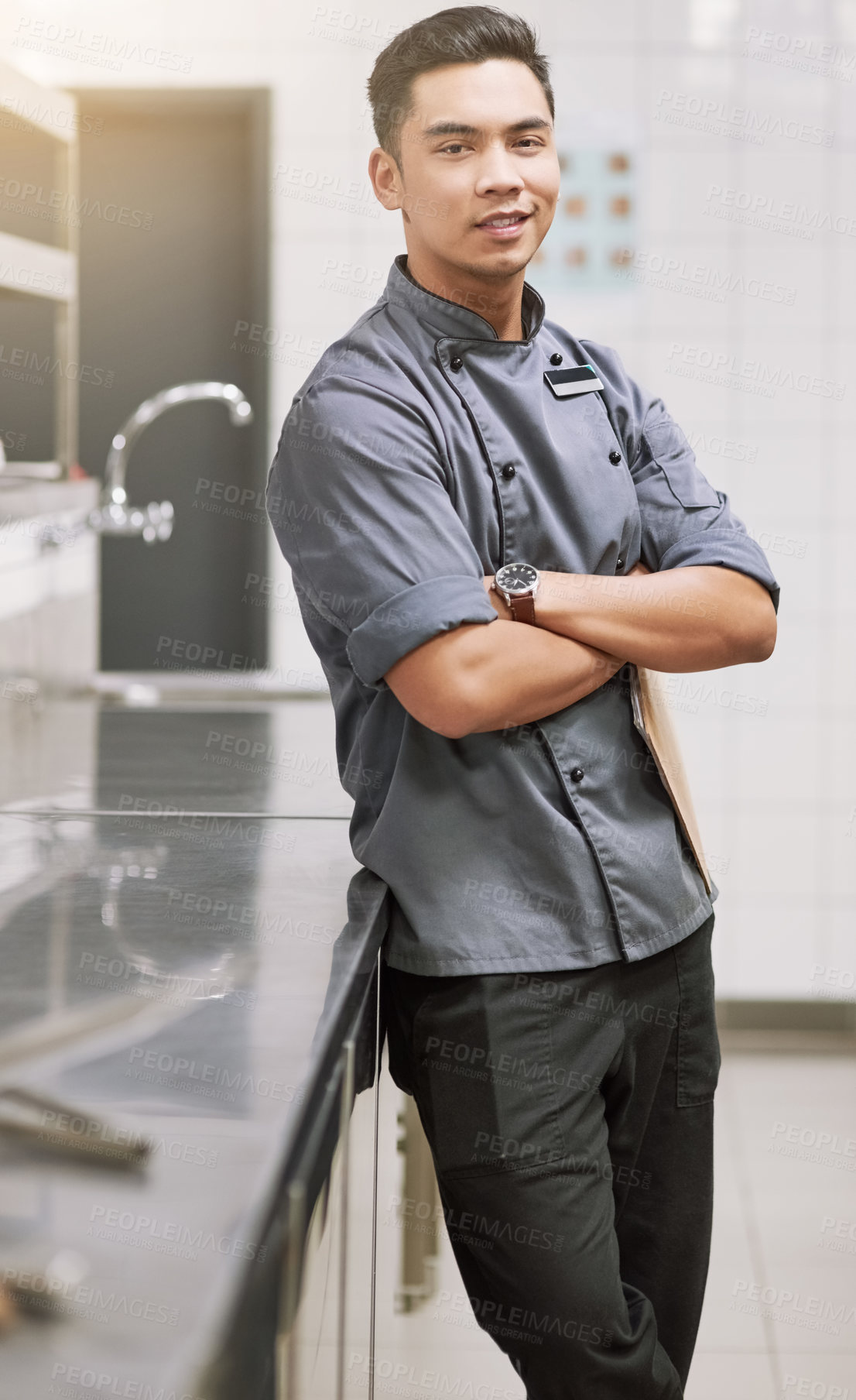 Buy stock photo Cropped portrait of a young male chef standing with his arms folded in the kitchen