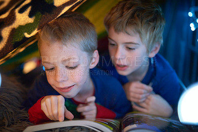 Buy stock photo Shot of two little brothers reading a bedtime story under their fort